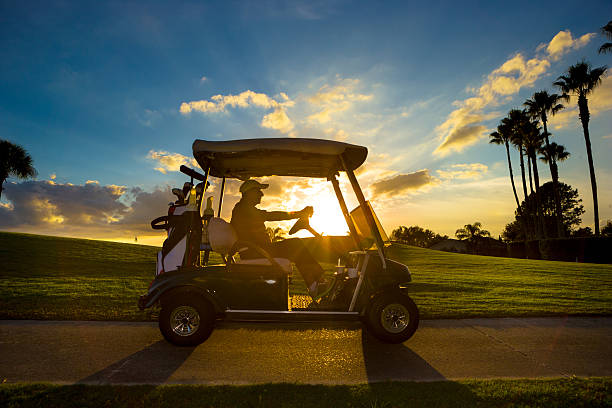 Golfer driving a golf cart along a cart path at sunset on a Florida course lined with palm trees.