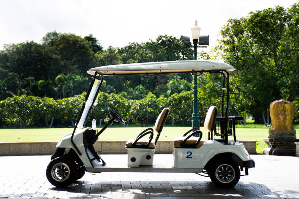 White four-seat golf cart parked on a paved path beside a green park lined with trees.